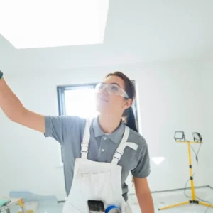 Femme peintre en bâtiment appliquant une peinture murale dans un chantier de rénovation