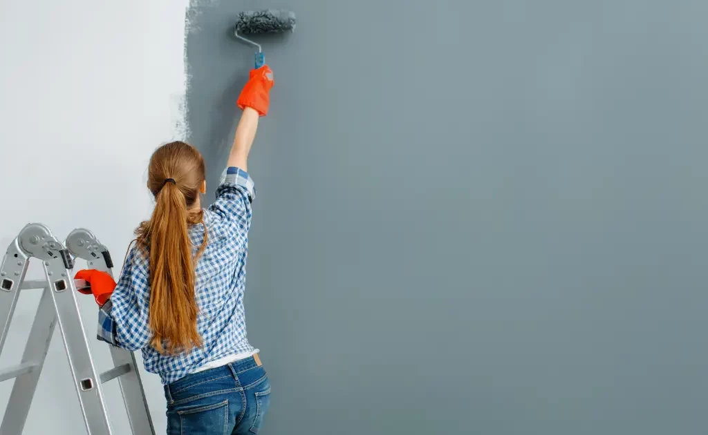 femme peintre en bâtiment appliquant de la peinture sur un mur intérieur