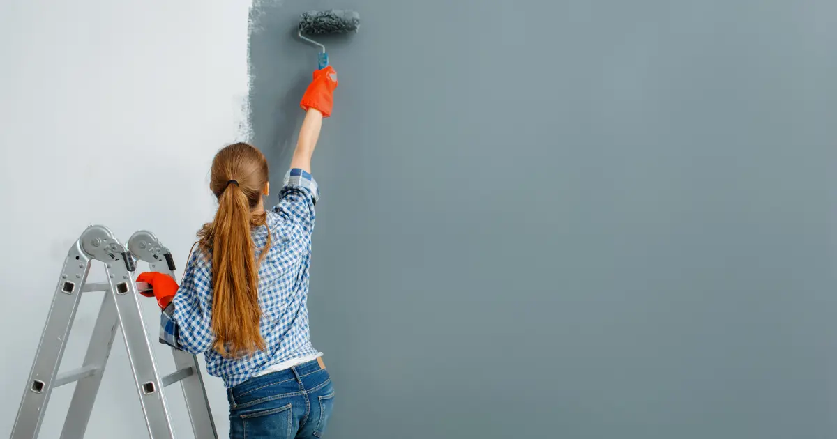 femme peintre en bâtiment appliquant de la peinture sur un mur intérieur