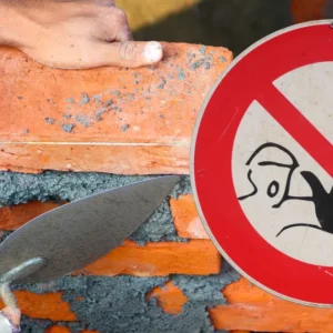 Maçon posant des briques sur un chantier avec un panneau de danger pour illustrer les erreurs de maçonnerie à éviter