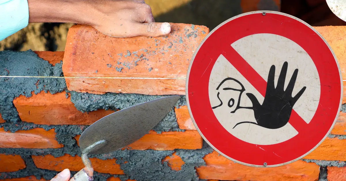 Maçon posant des briques sur un chantier avec un panneau de danger pour illustrer les erreurs de maçonnerie à éviter