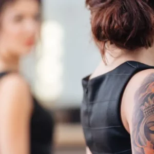 Femme tatouée face à un miroir, symbole de la culture du tatouage et réseaux sociaux en 2025